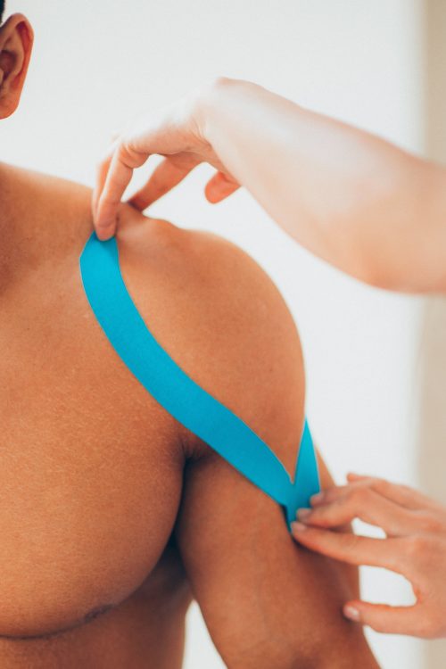 Physical therapist placing kinesio tape on patient's shoulder